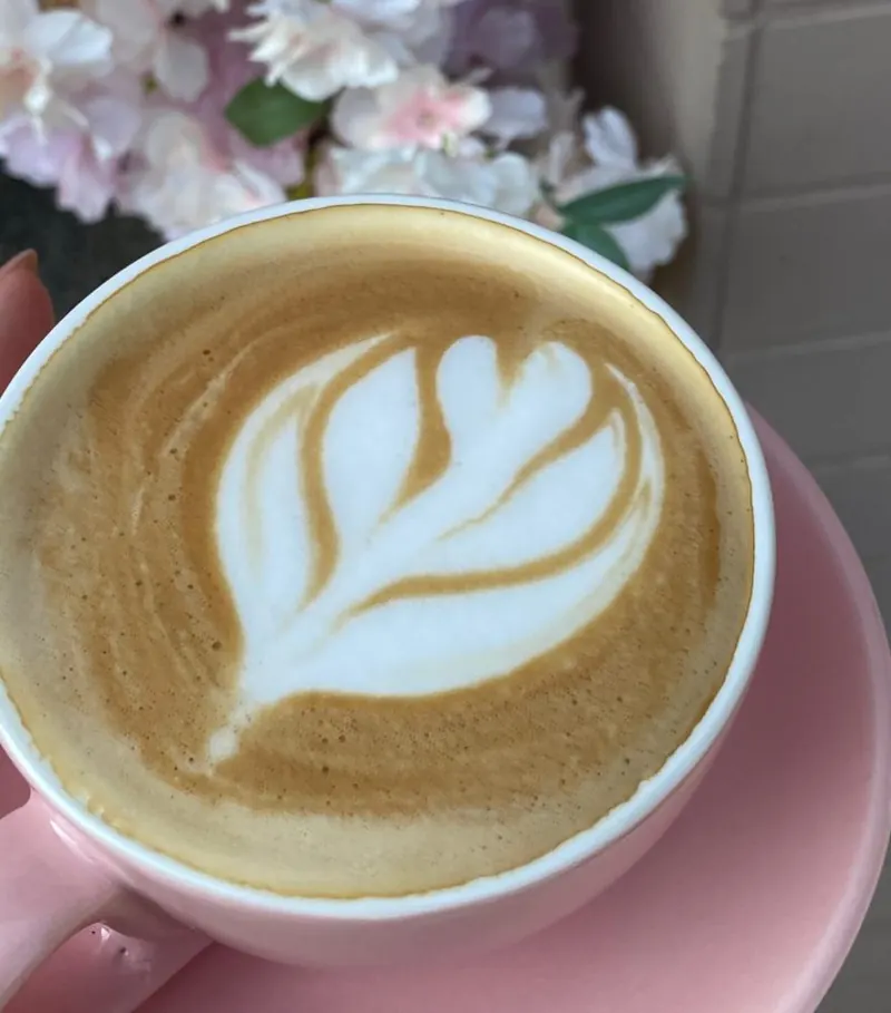 Cappuccino s latte art v ružovej šálke pri kvetinovej stene